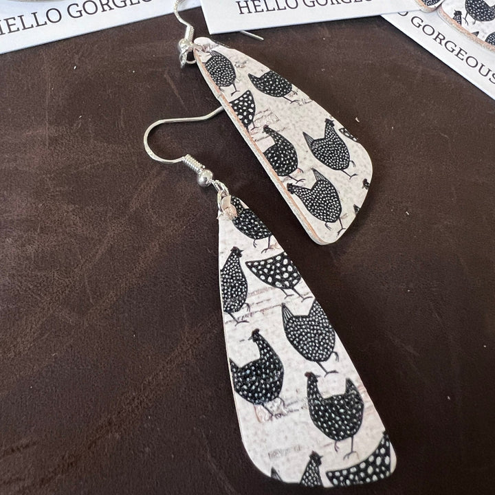 Close up photo of long angle earrings with white background with black chicken print