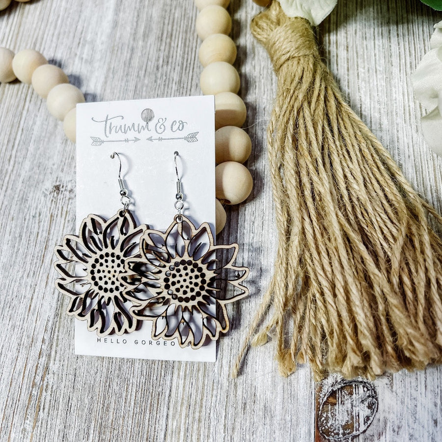 Lightweight earrings of Birch laser cut sunflowers on a trumm and co earring card laying on a peice of wood