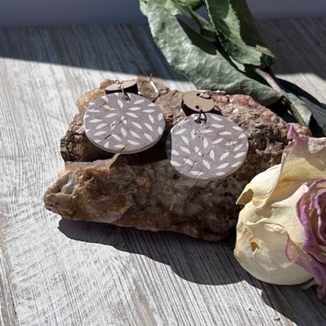 different angle of ashy taupe circle dangle earrings on a rock outside