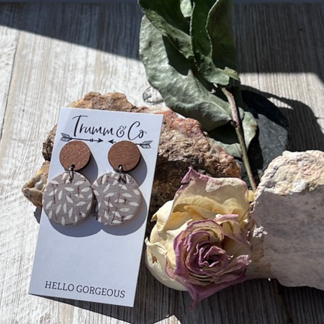 aightweight earrings, wood stud piece with cork leather ashy taupe color with ivory mum print on a Trumm & Co earring card leaning on a rock