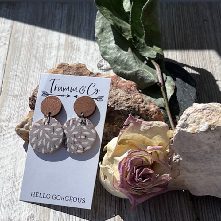 aightweight earrings, wood stud piece with cork leather ashy taupe color with ivory mum print on a Trumm & Co earring card leaning on a rock