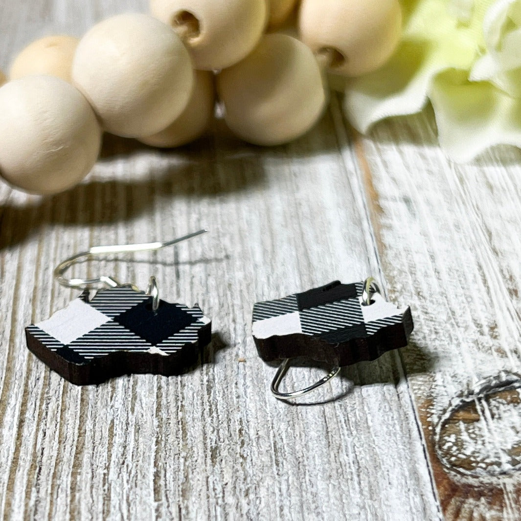 Close up photo of black and white Wisconsin shaped dangle earrings laying on whitewash board, made by Trumm & Co